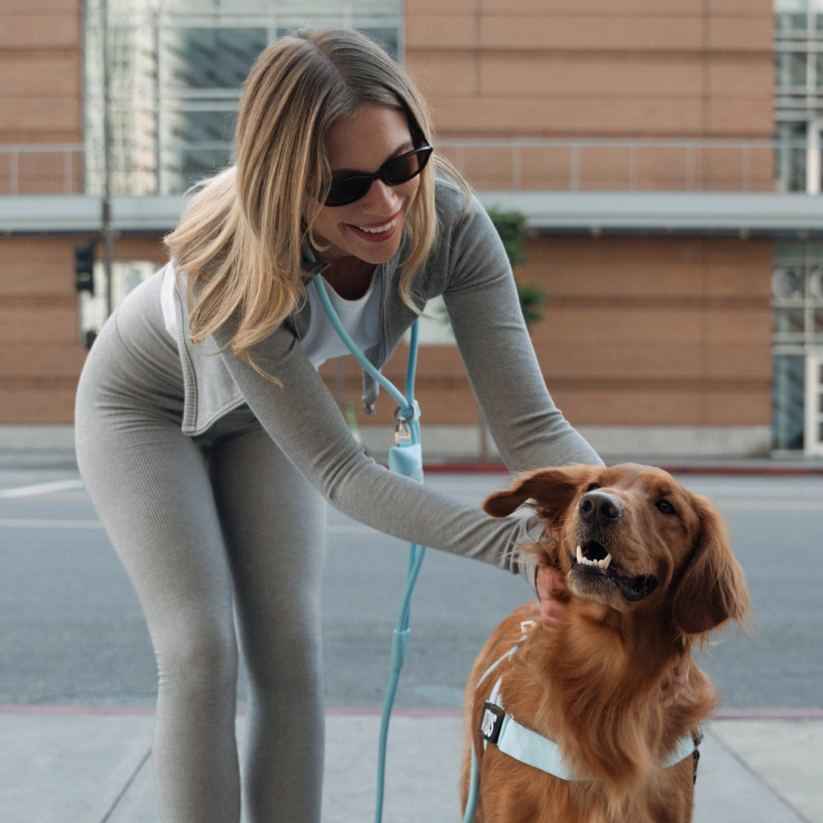 Dog owner wearing the Sky Blue hands-free leash while standing beside a brown dog wearing a Sky Blue harness.