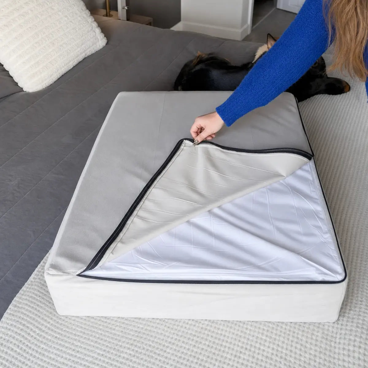 A hand unzipping the bed cover to show the white waterproof liner over the foam